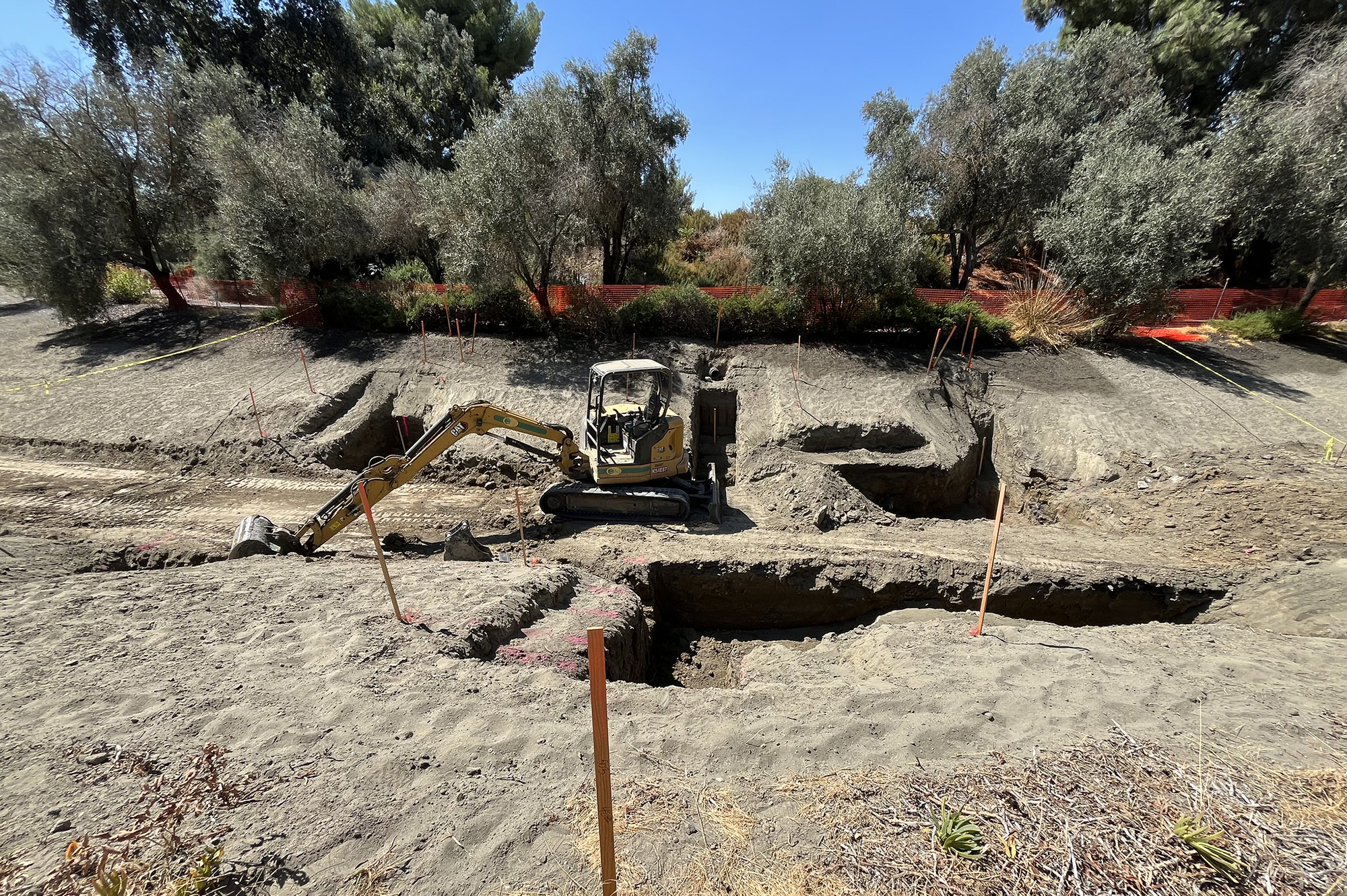 The drained waterway shows an expanse of dirt, an excavator is in the middle digging holes throughout.
