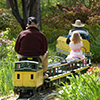 Image of two adults and a child on small train winding through a garden.
