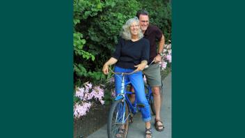Kent Bradford and Barbara Zadra posing together on a bike in their garden.