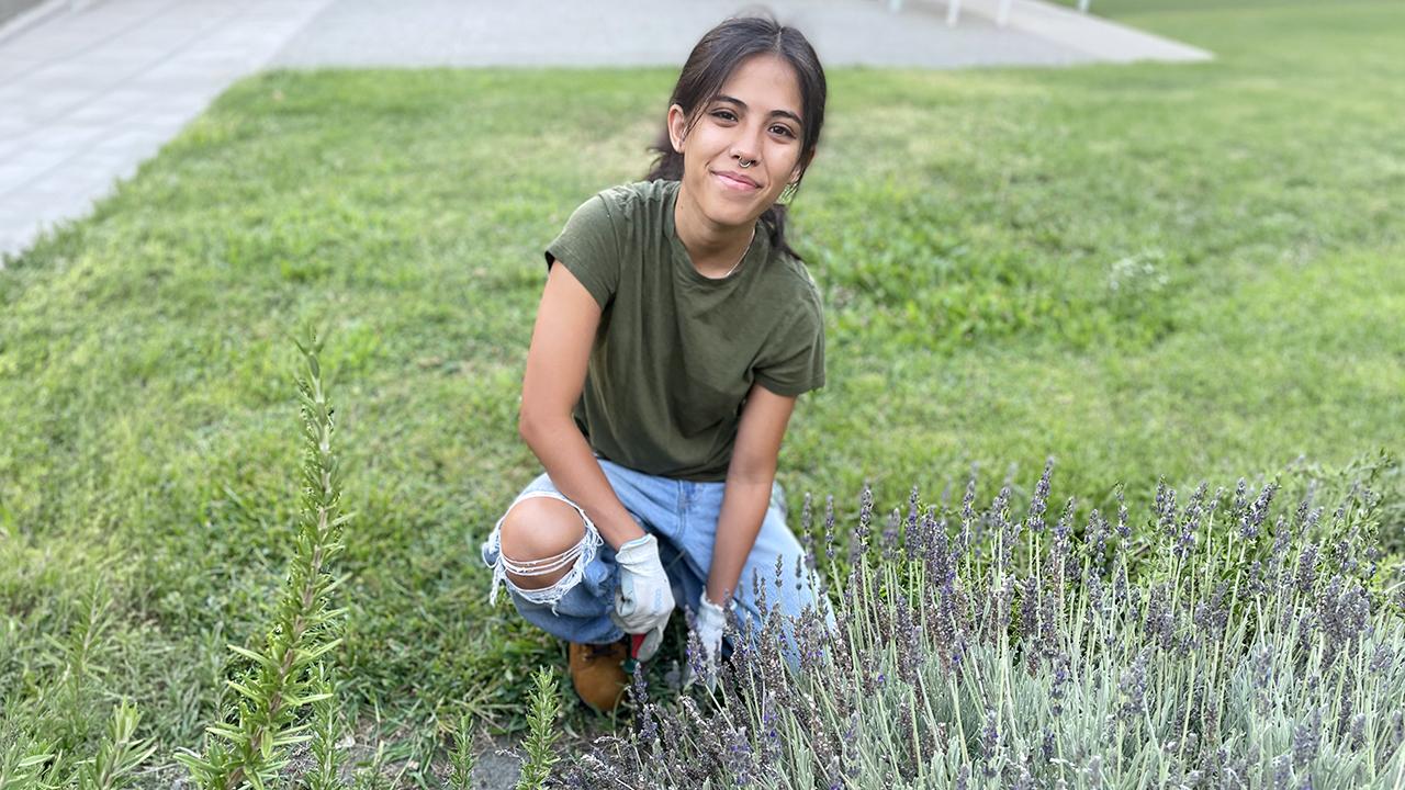 A student kneeling by a lavender patch and smiling.