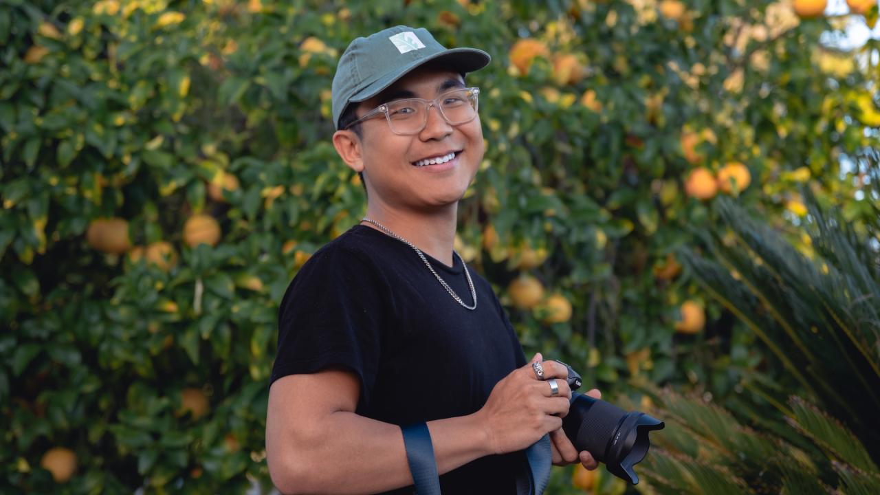 Matthew poses, smiling and holding a camera