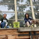 Two people smiling, kneeling in a garden bed pulling weeds
